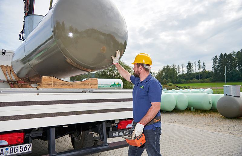 Mann mit gelbem Helm und blauer Arbeitskleidung lädt einen großen Flüssiggasbehälter auf einen weißen LKW