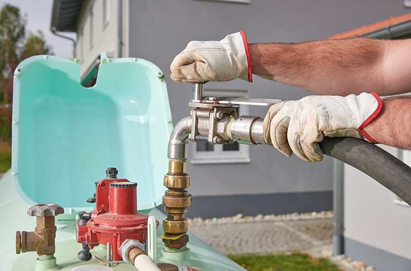 Person mit Arbeitshandschuhen schließt Schlauch zum Befüllen an Ventil eines grünen Gastanks an