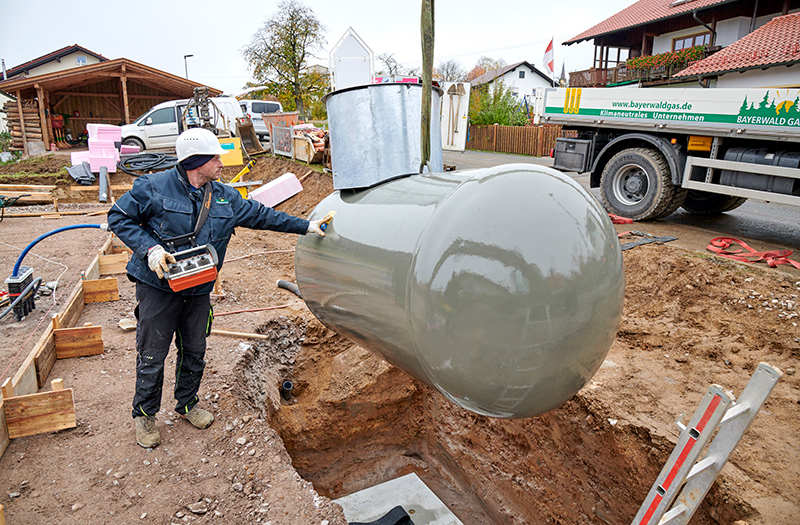 Arbeiter setzt großen grauen Flüssiggasbehälter in eine Baugrube auf einer Baustelle ein